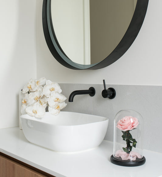 A pink eternal rose in a dome in a bathroom with an orchid