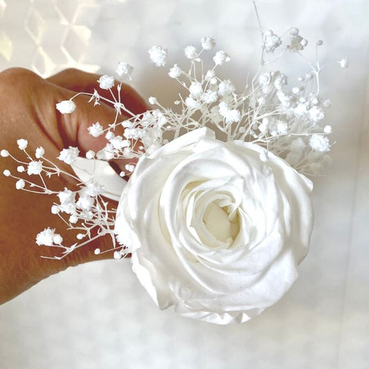 Single white rose arranged for wearing in a suit button hole. Arrangement also contains white babys breath flowers.