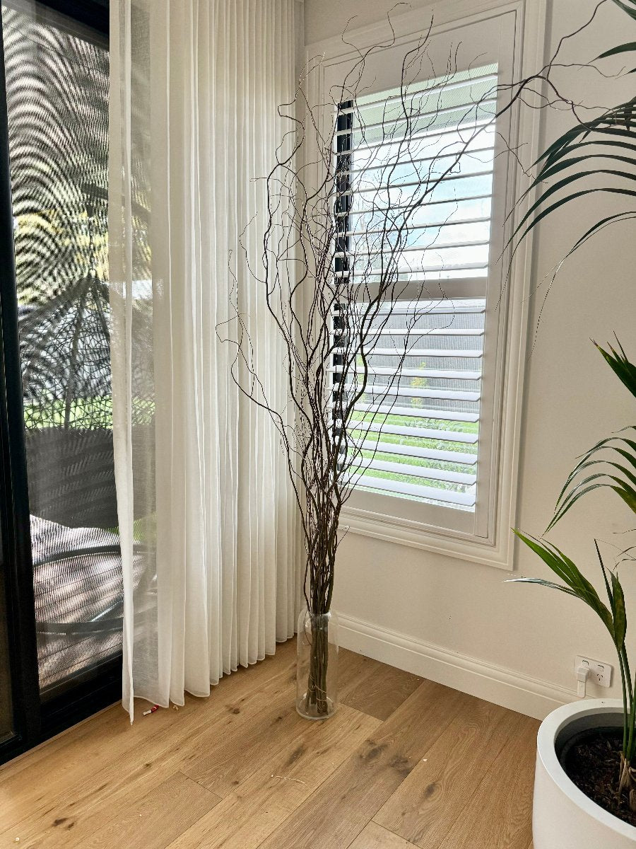 branches in the corner next to white curtains