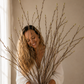 Woman holding a bundle of branches indoors with a neutral background