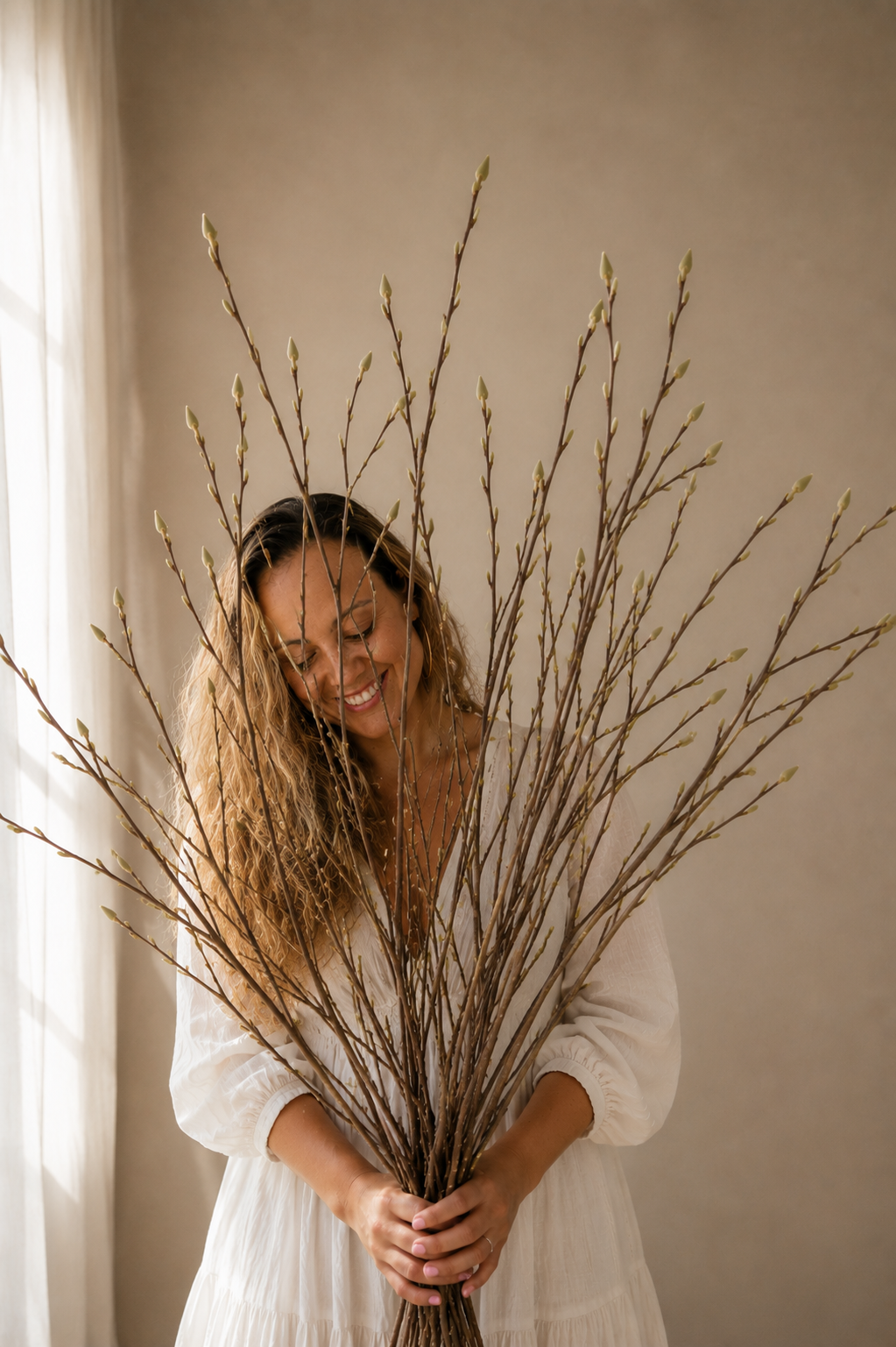 Woman holding a bundle of branches indoors with a neutral background