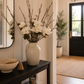 Decorative vase with faux magnolia white flowers combined with real branches on a console table in a home entryway.