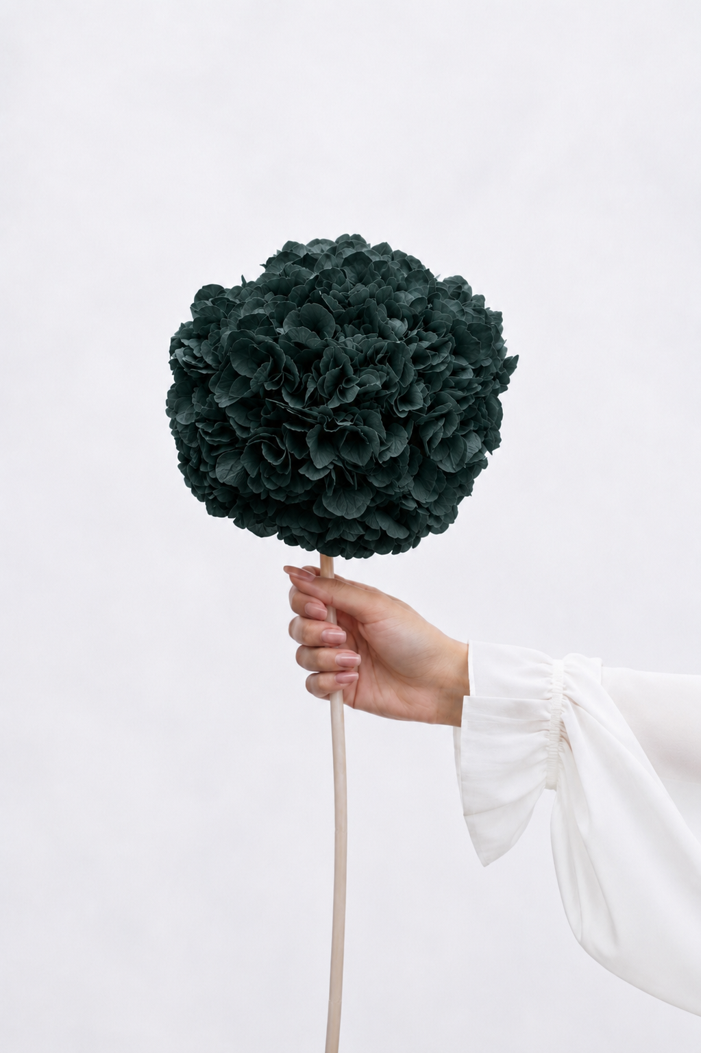 Hand holding a dark green decorative flower ball against a light background