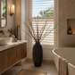 Bathroom with a large vase of branches on a windowsill, a bathtub, and a vanity.