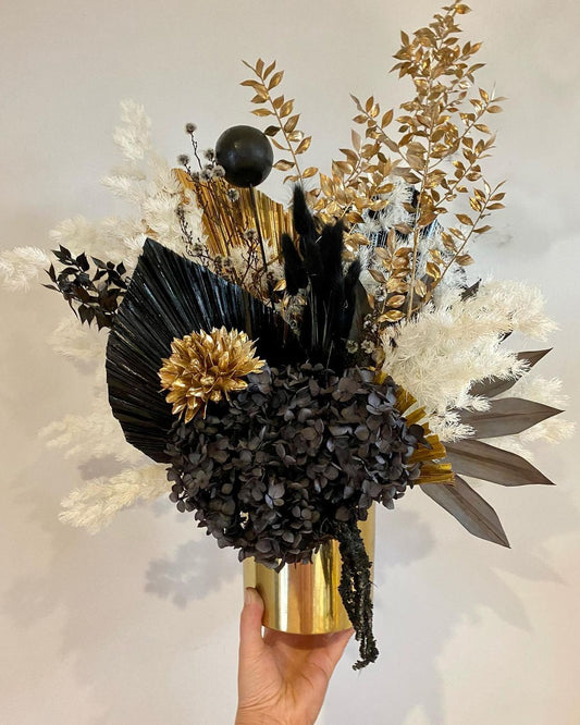 A Gold and Black flower arrangement in a gold vase