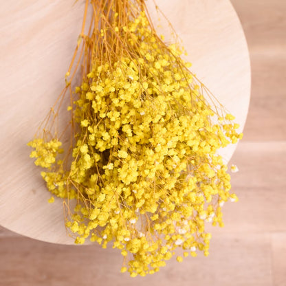 Bunch of preserved babys breath displayed on a light wooden back drop. The babys breath is dyed bright yellow.